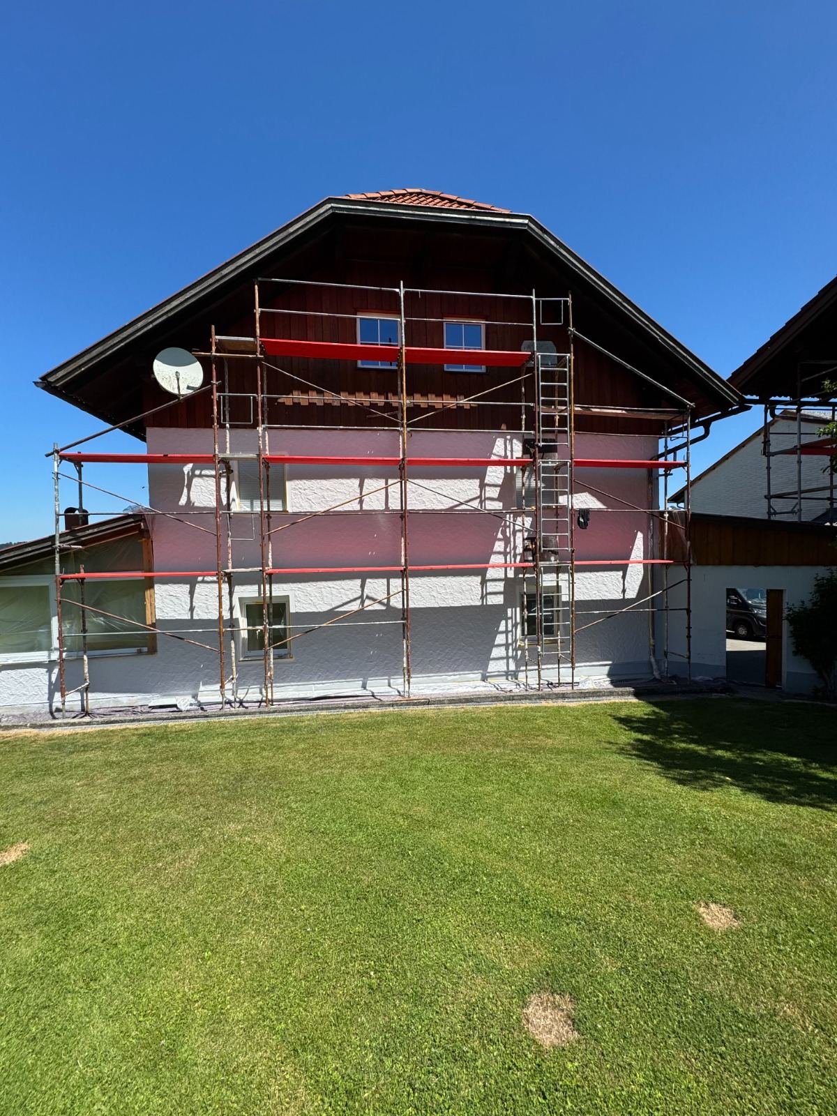 Eingerüstetes Haus mit rotbrauner Fassadenbeschichtung