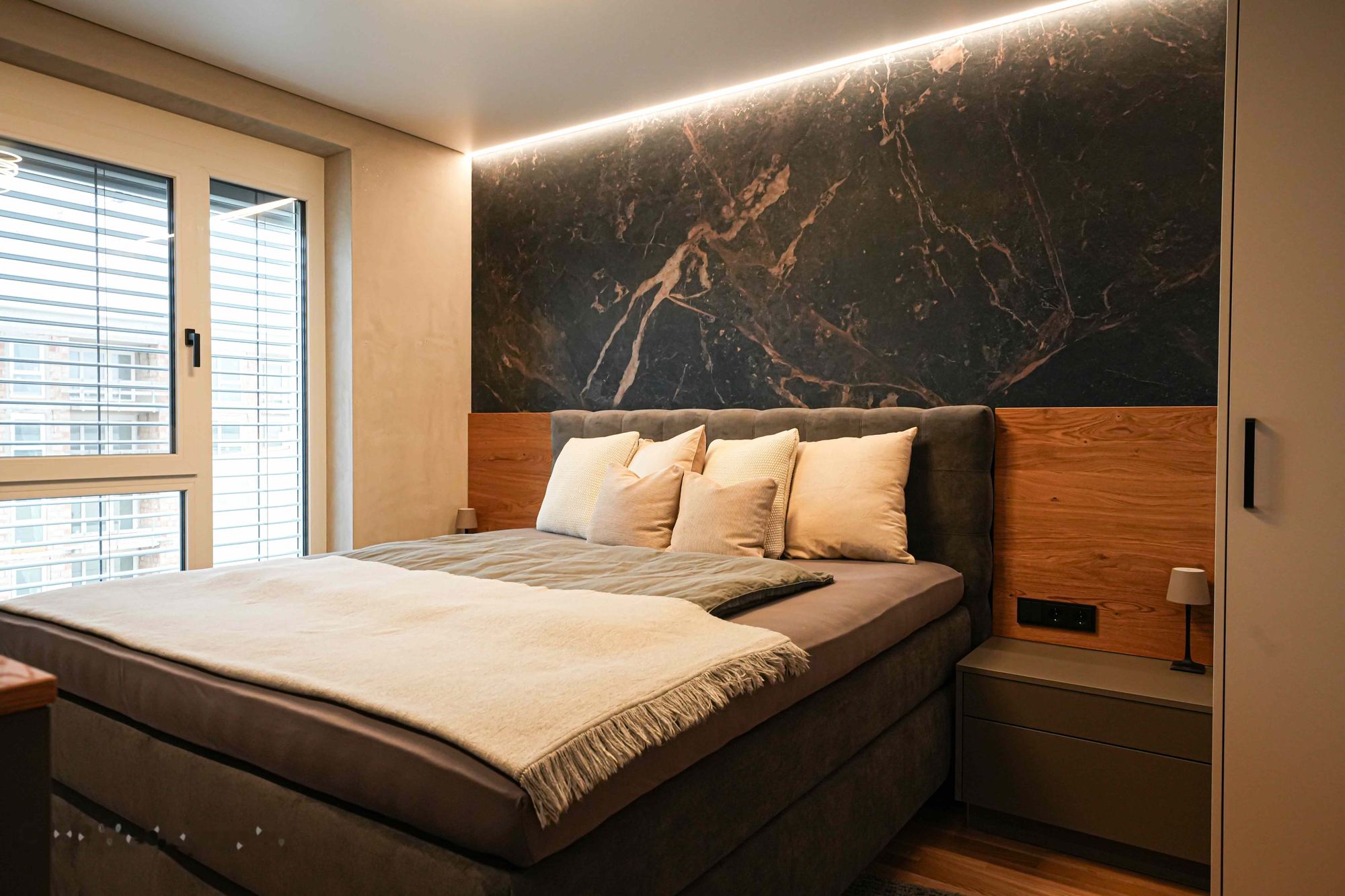 Schlafzimmer mit dunkler Marmoroptik, Holz und indirektem Licht