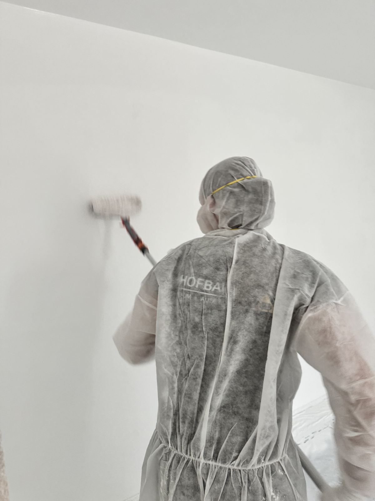 Hofbauer-Mitarbeiter im Schutzanzug rollt eine weiße Wand