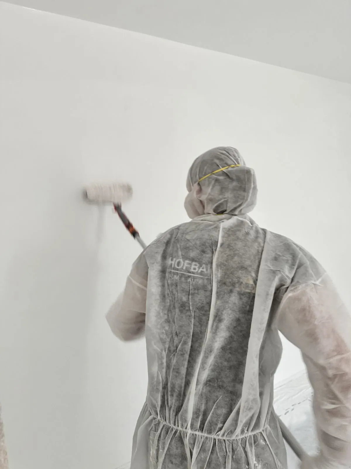 Hofbauer-Mitarbeiter im Schutzanzug rollt eine weiße Wand